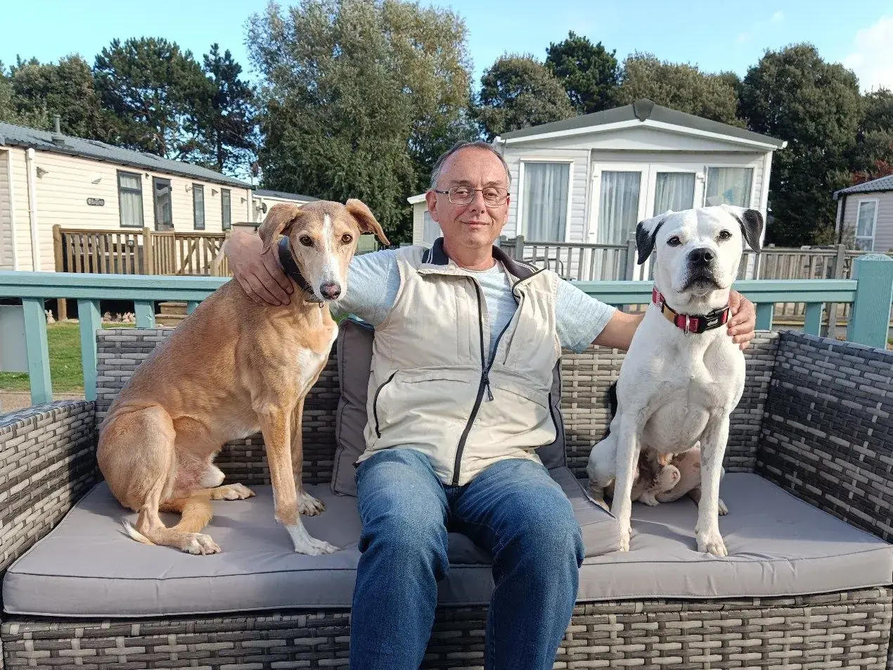 Guest sitting on the Tern 32 deck sofa with two dogs beside him, turquoise railings and caravans behind