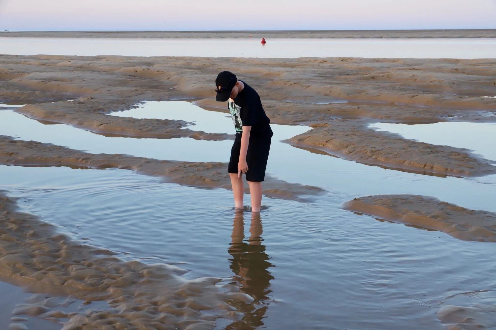 A young guest paddling in a shallow pool on the tidal flats at dusk, with wide empty sands around