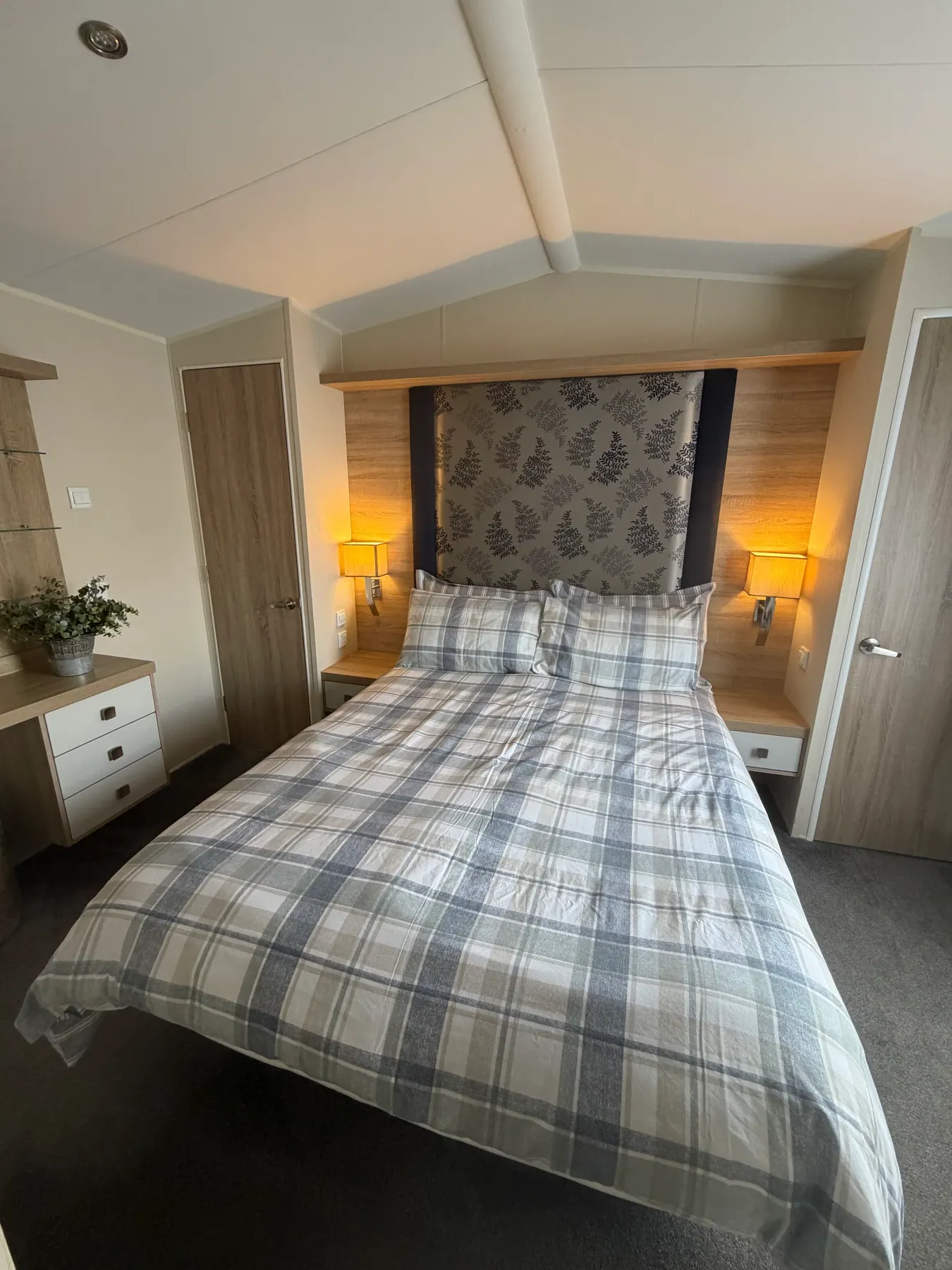 King-size bedroom inside Tern 32 with blue-and-white plaid bedding, a patterned headboard panel, bedside lamps, wooden bedside tables and a chest of drawers