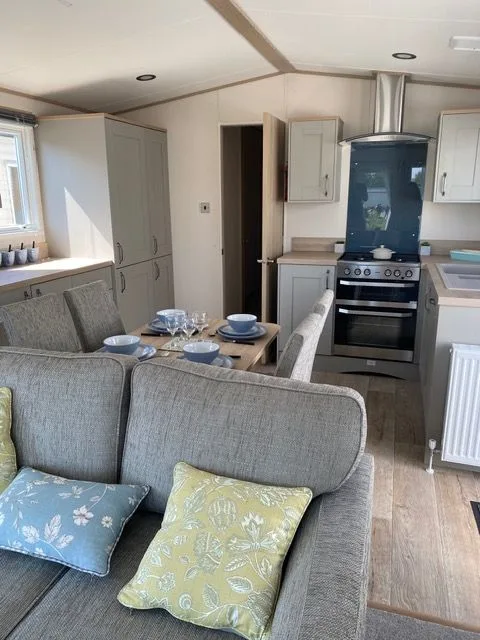 The kitchen and dining area inside Windsor 30, seen from the sofa, with a table laid for four, grey units, a range-style oven and an extractor hood