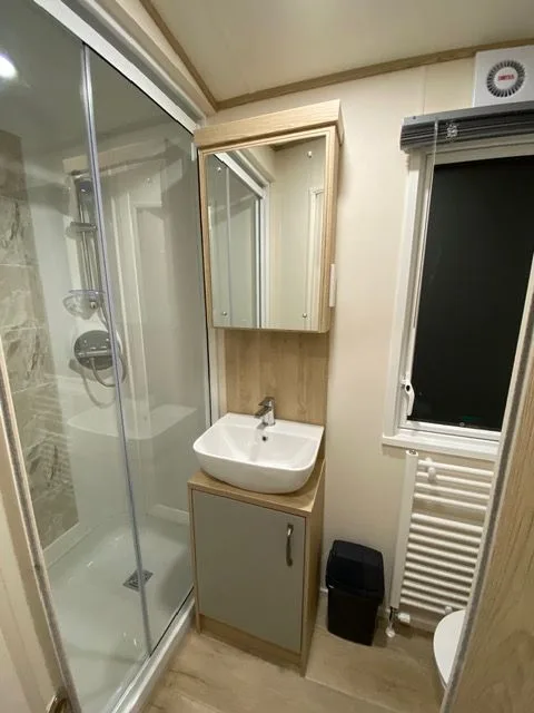 The shower room inside Windsor 30 with a glass shower cubicle, a basin on a grey vanity unit, a mirrored cabinet and a heated towel rail